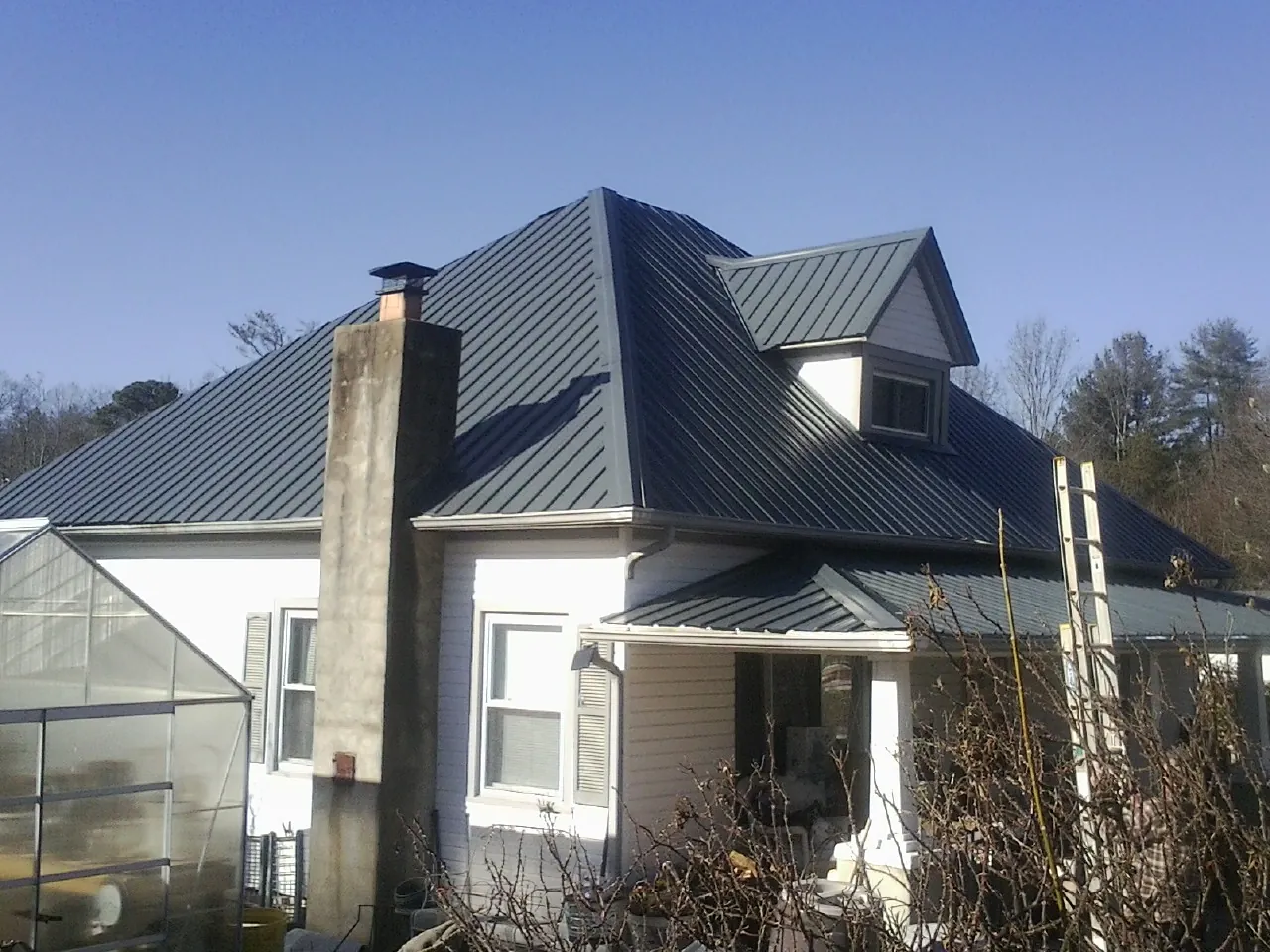 Dark blue standing seam metal roof on a white farmhouse with dormer — Slate & Tile Roof Repair by Roofing Brothers in Spicewood