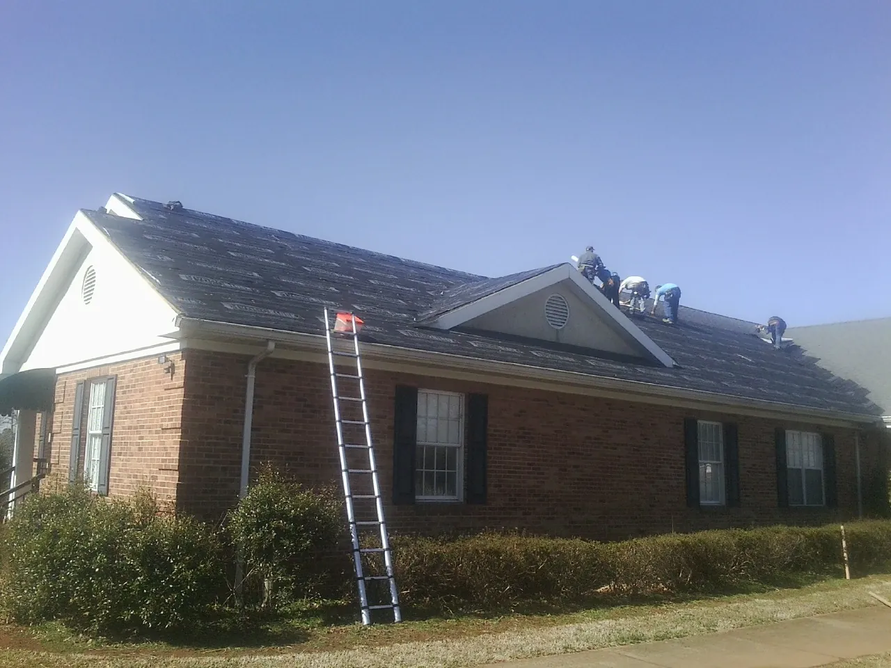 Crew tearing shingles off a brick ranch roof with a ladder set — Emergency Roof Repair work by our crew in Spicewood
