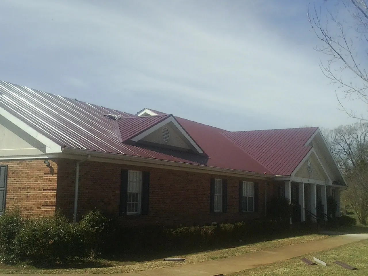 Red metal roof with gabled entries on a long brick building, from a Hail Damage Roof Repair job in Spicewood