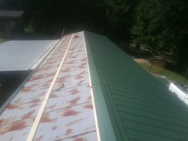 Old rusted panels beside newly installed green metal roofing — Wind Damage Roof Repair by Roofing Brothers in Spicewood