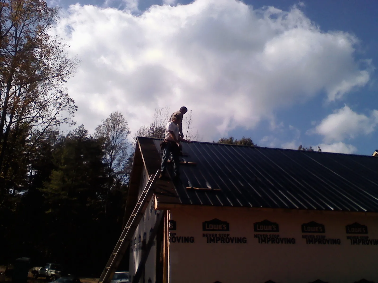 Roofer fastening dark metal panels high against a cloudy sky, from a Roof Inspection job in Spicewood