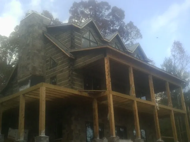 Stone chimney and dormers on a large log home with a timber porch in Spicewood