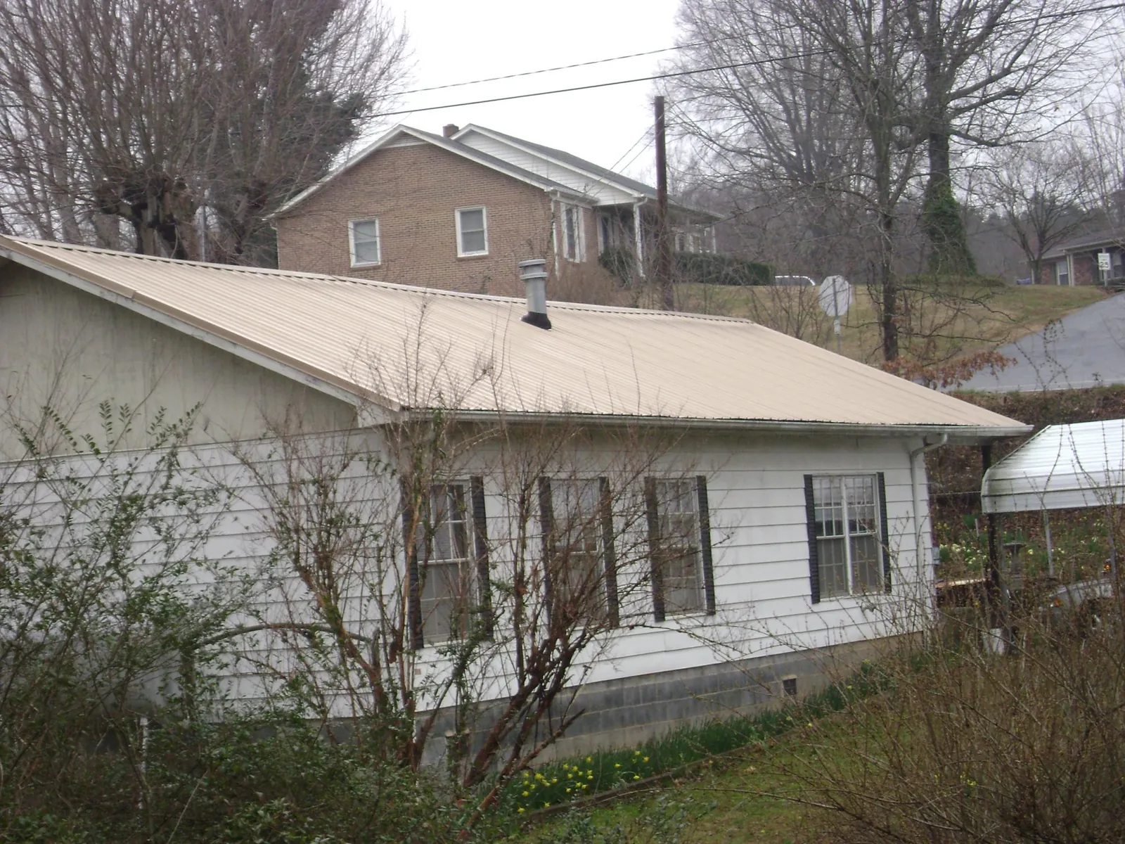 Tan metal roof on a white sided house set into a hillside — Commercial Roofing by Roofing Brothers in Spicewood